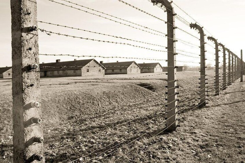 A barbed wire fence with barbed wire on top, a concrete post, and a building in the background. 4