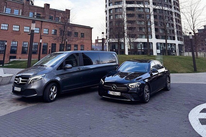 Two cars parked on a paved area with buildings in the background. 2
