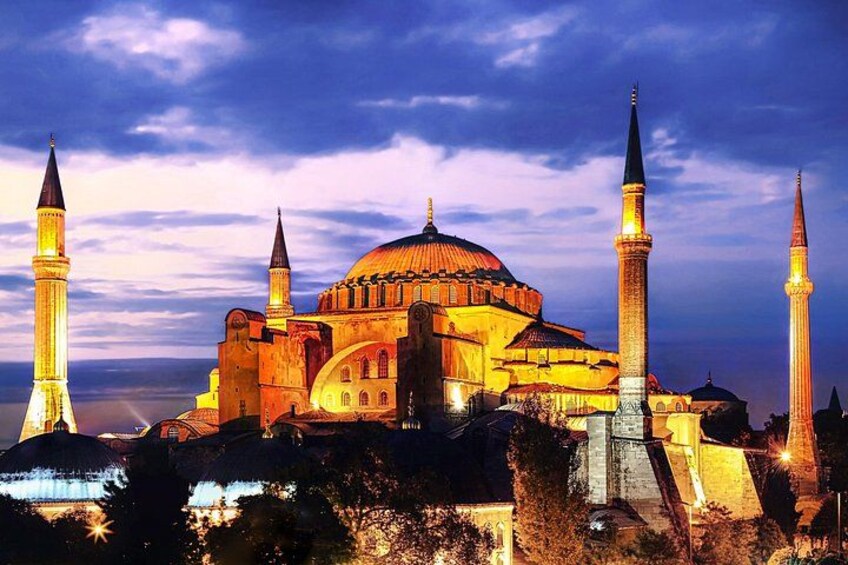 A historic building with a large central dome and four minarets, illuminated at dusk. 1