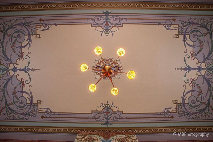 A ceiling with a central chandelier and ornate floral patterns. 2