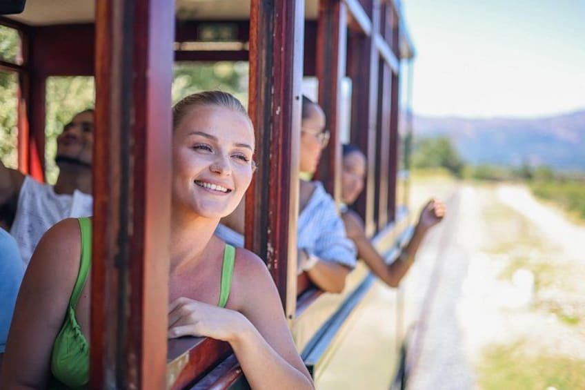 A train with passengers, a clear sky, and a road with mountains in the background. 1