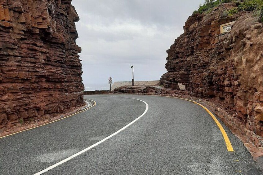 A winding road flanked by steep rock cliffs, a no-overtaking sign, and a sign indicating a tourist attraction. 2