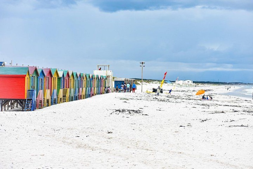 Een strand met kleurrijke strandhutten, een uitkijktoren van de badmeester, en mensen in de verte. 3