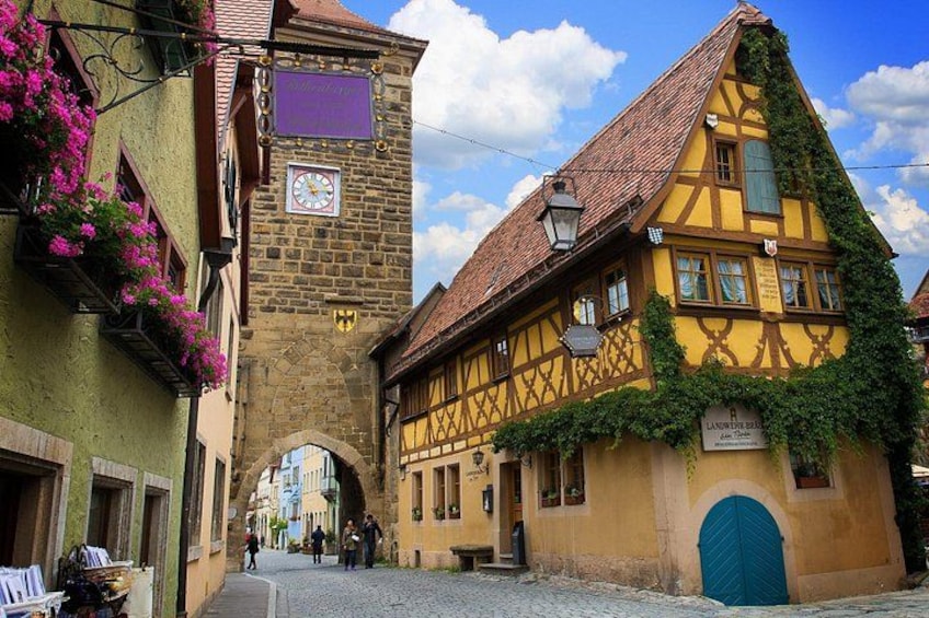 A cobblestone street with traditional half-timbered houses, a clock tower, and a blue door. 3