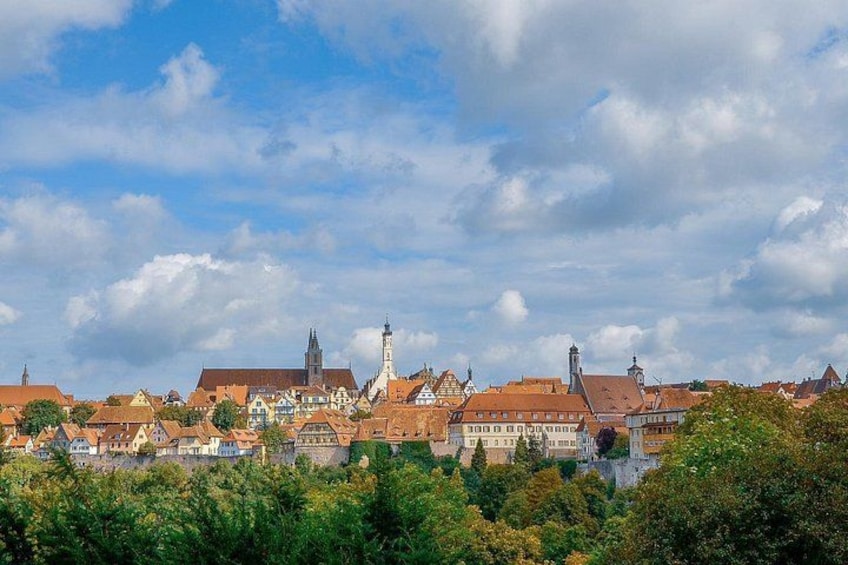 A town with historic buildings, a prominent church tower, and a castle in the background. 2