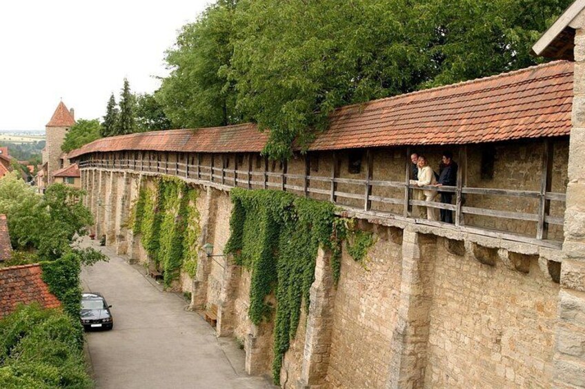 A stone wall with ivy, a paved road, and a distant tower. 1