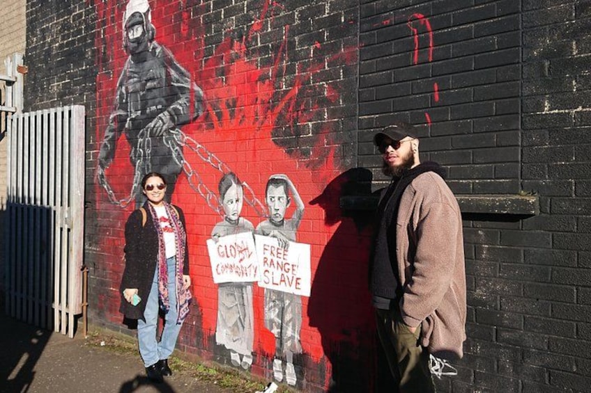 A mural on a brick wall, a person holding a sign, and another person standing beside them. 4