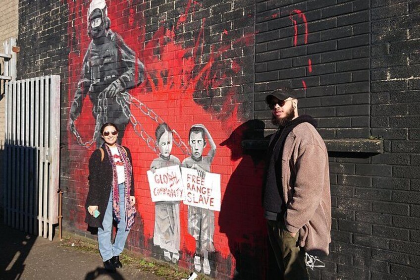 A mural on a brick wall with a figure in a gas mask, a person holding a sign, and another person standing beside them. 4