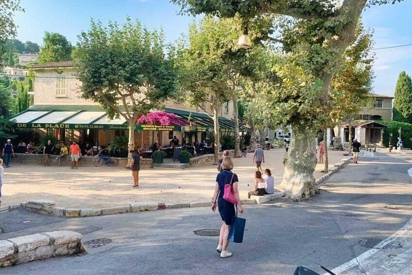 A public square with people walking, a café with outdoor seating, and trees lining the area. 2