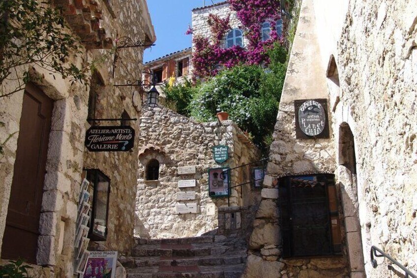 A narrow stone street with signs for an artist's gallery and a café. 5