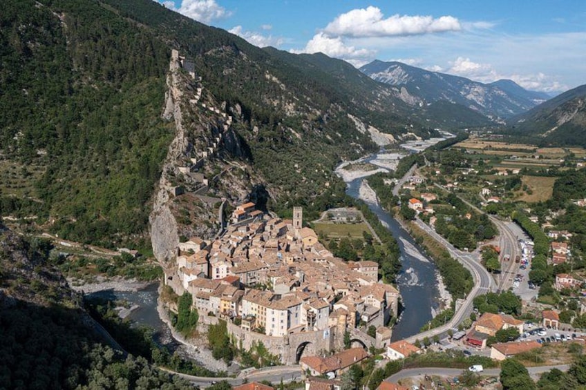 Un pueblo montañoso con un río, un camino sinuoso y una imponente construcción que parece un castillo. 5