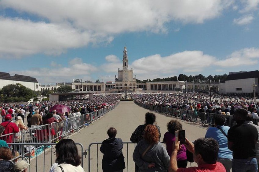 A large crowd gathered in a public square, facing a prominent building with a tall tower. 1
