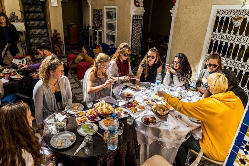 A group of people dining at an outdoor table with various dishes and drinks. 1