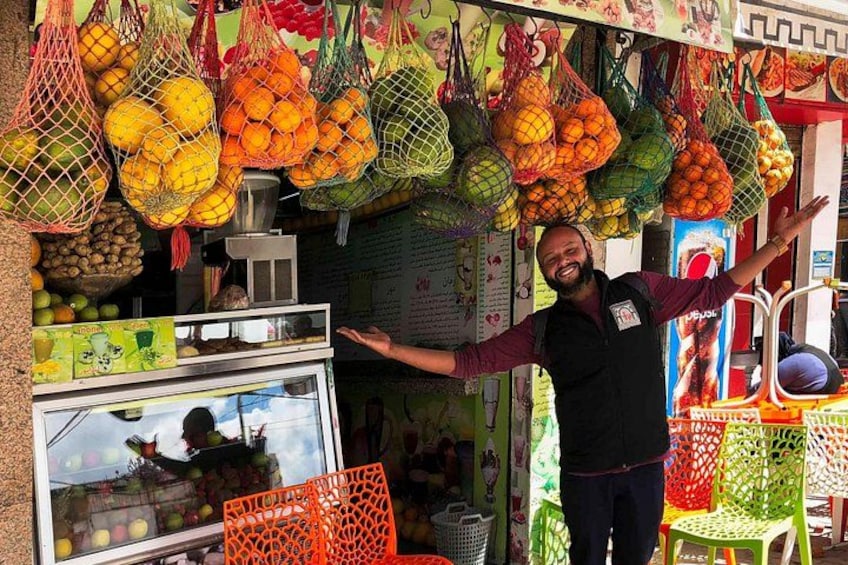 A fruit vendor with bags of oranges and other fruits, a display case, and colorful chairs. 2