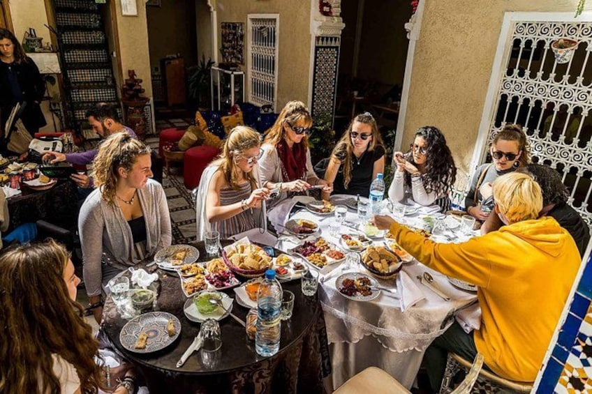 A group of people dining at an outdoor table with various dishes and drinks. 1