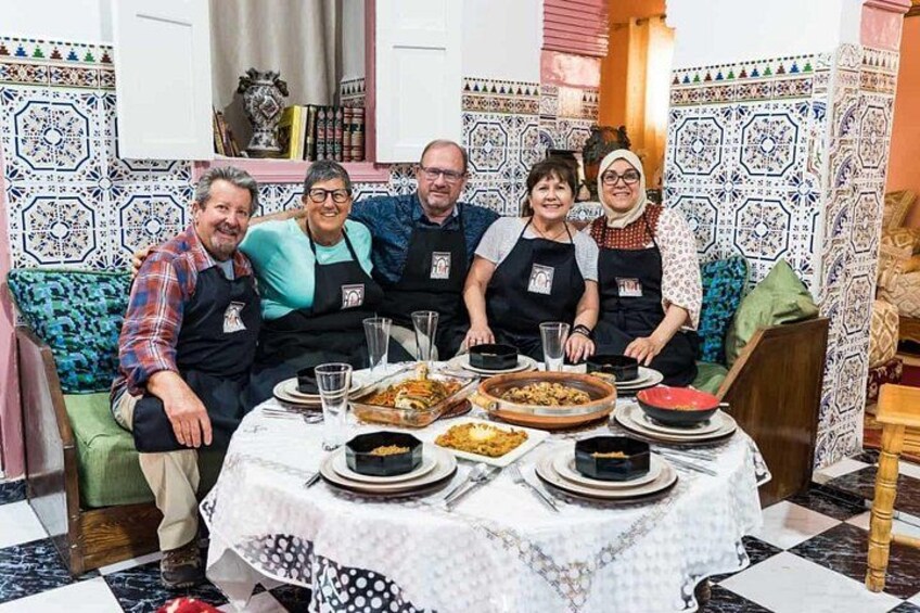 Un groupe de personnes est assis autour d’une table, devant divers plats, dans une pièce aux carreaux décoratifs et au décor traditionnel. 1