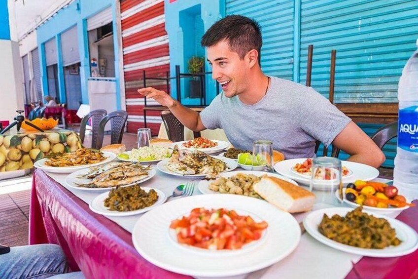 Una persona sentada en una mesa al aire libre con diversos platos, entre ellos ensaladas, carnes y pan, en un ambiente de restaurante informal. 2