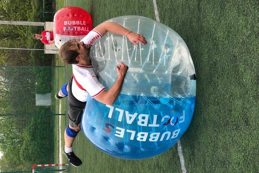 Een persoon speelt bubbelvoetbal op een veld van groene kunstgras. 3