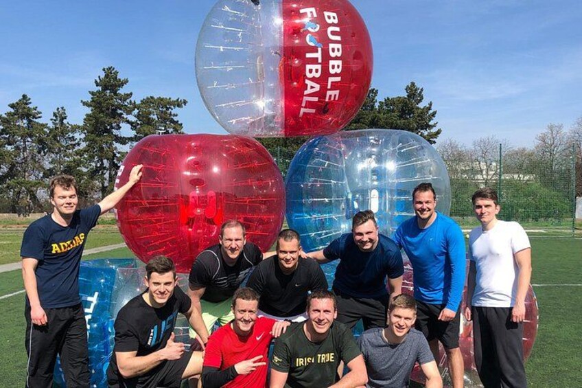Een groep mensen die poseren met grote, doorzichtige voetbalvormen, voorzien van de tekst 'BUBBLE FOOTBALL', op een grasveld. 5
