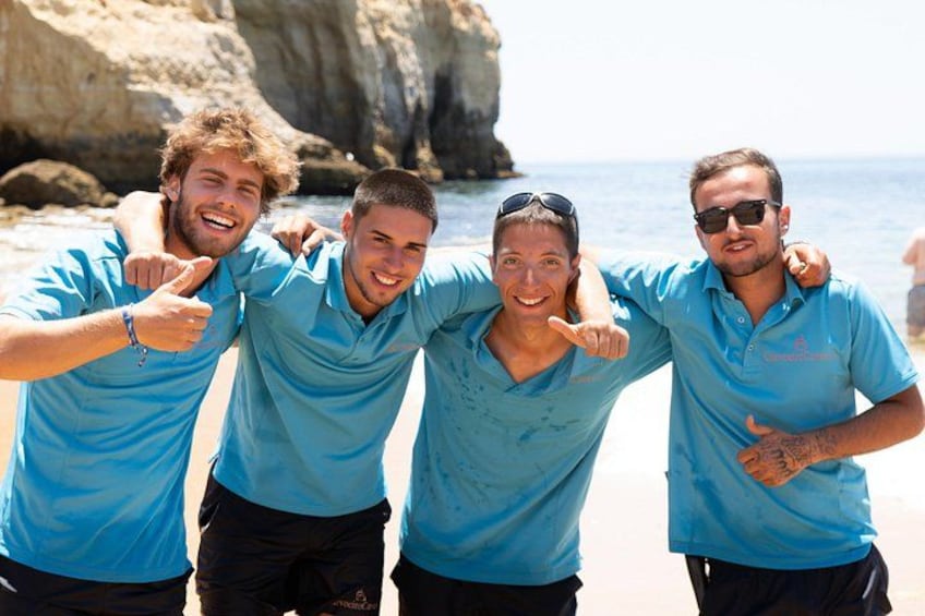 Four people in blue shirts on a beach with a rocky cliff in the background. 3