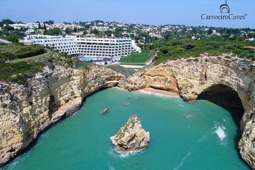 A coastal landscape with a large rock arch formation, clear turquoise waters, and a hotel in the background. 5