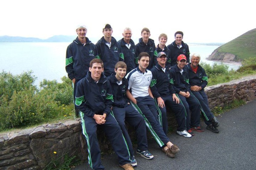 A group of people in sports attire by a coastal road with a stone wall and grassy area. 2