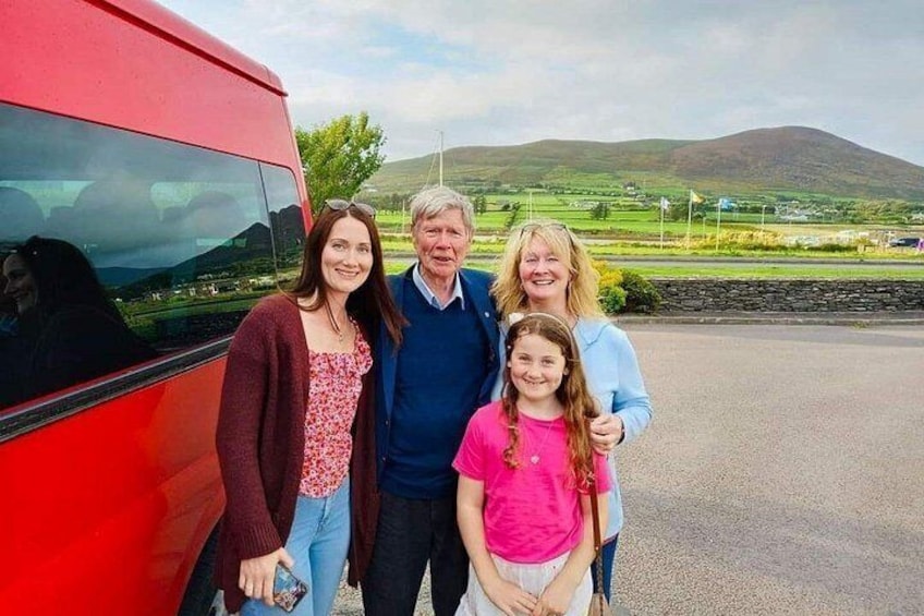 A family of four standing in front of a red bus with a scenic landscape in the background. 1