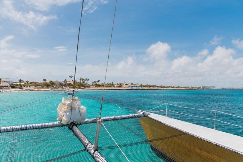 A boat's deck with a view of the turquoise sea and a distant shoreline with buildings and palm trees. 1