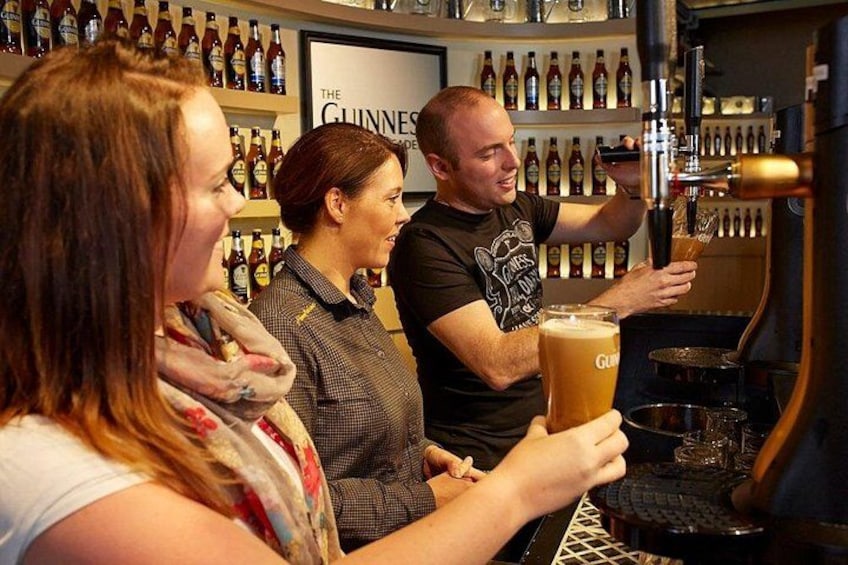 A bar setting with a person pouring beer into a glass, a shelf with bottles, and a Guinness sign in the background. 2