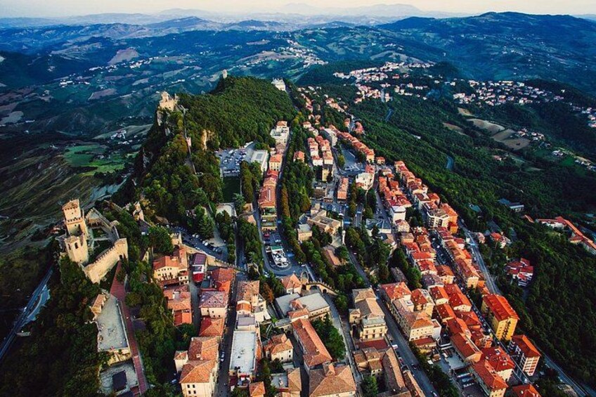 A town nestled in a valley with a prominent castle on a hill, surrounded by lush greenery and a mix of traditional and modern buildings. 4