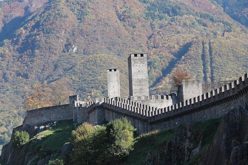 Un castillo medieval con una muralla alta y dos torres, rodeado por un paisaje montañoso. 4