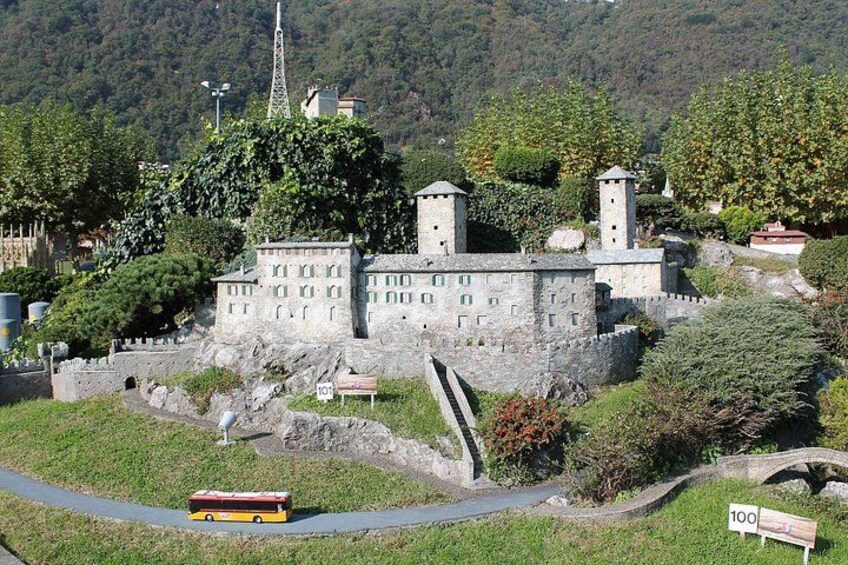 Un castillo con torres, rodeado de vegetación y una carretera con un autobús. 1