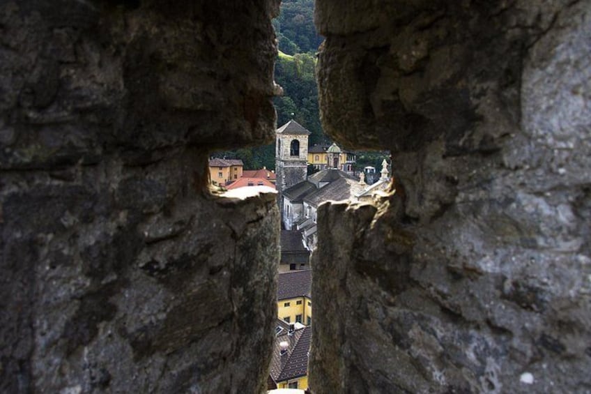 Vista a través de un arco de piedra sobre un pueblo con edificios y una iglesia. 3