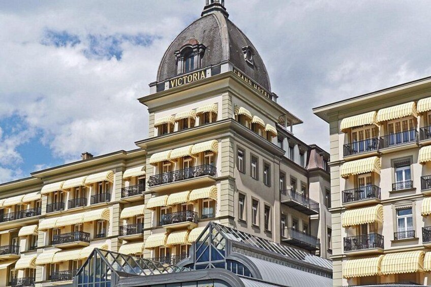 Un edificio storico con una cupola con la scritta 'VICTORIA HOTEL' e numerosi balconi con tende da sole gialle. 3