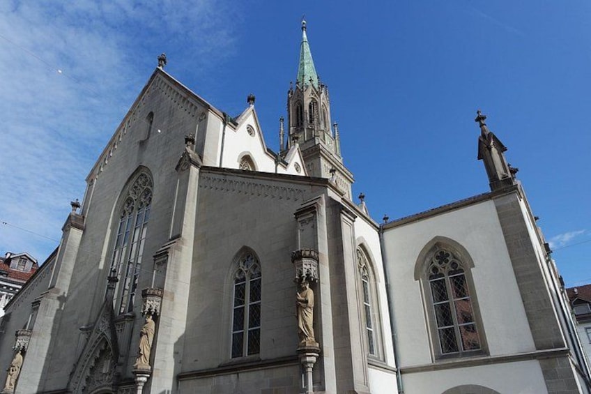 Een historisch kerkgebouw met een hoge spits, gebogen ramen en beelden. 5