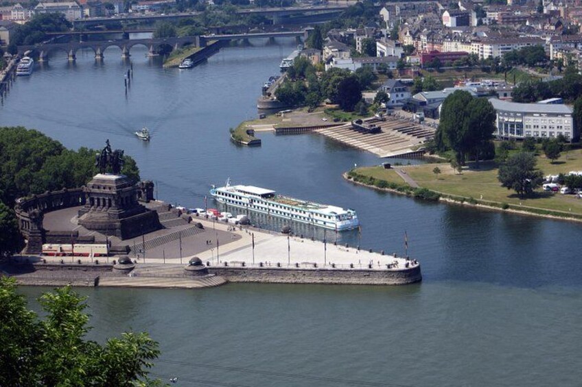 A river with a large cruise ship docked at a pier, surrounded by buildings and greenery. 4