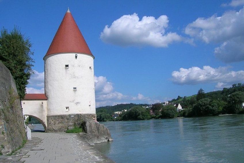 A white tower with a red roof by a river, surrounded by greenery and houses. 2