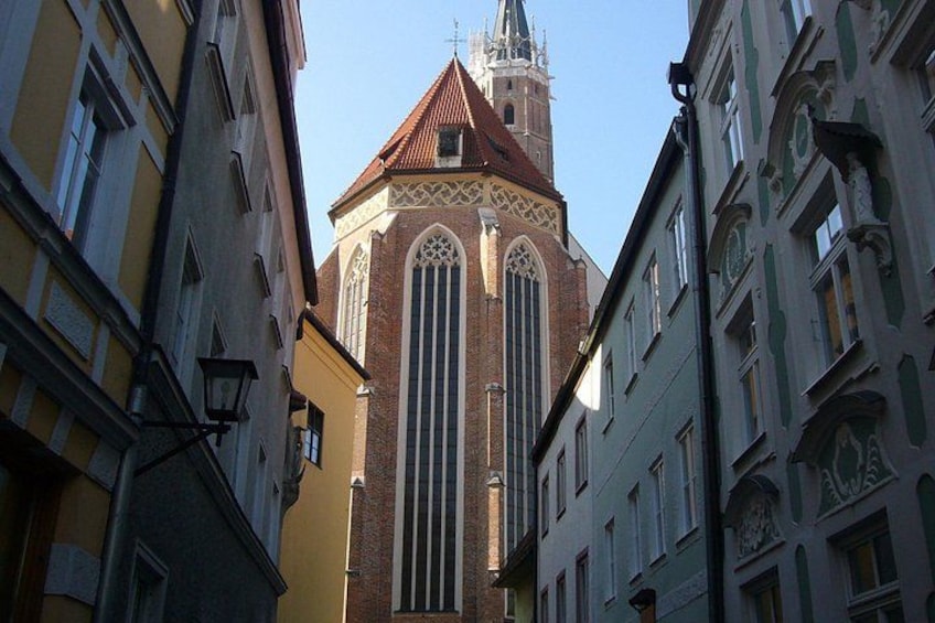 A church with a tall tower and a red roof, surrounded by buildings with arched windows and decorative elements. 4