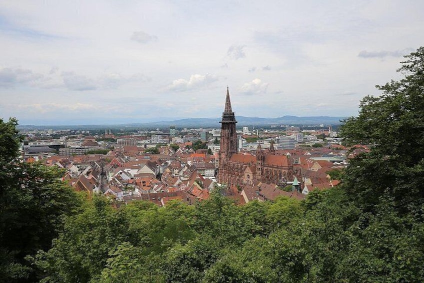 A cityscape with a prominent church tower, dense urban buildings, and surrounding greenery. 5
