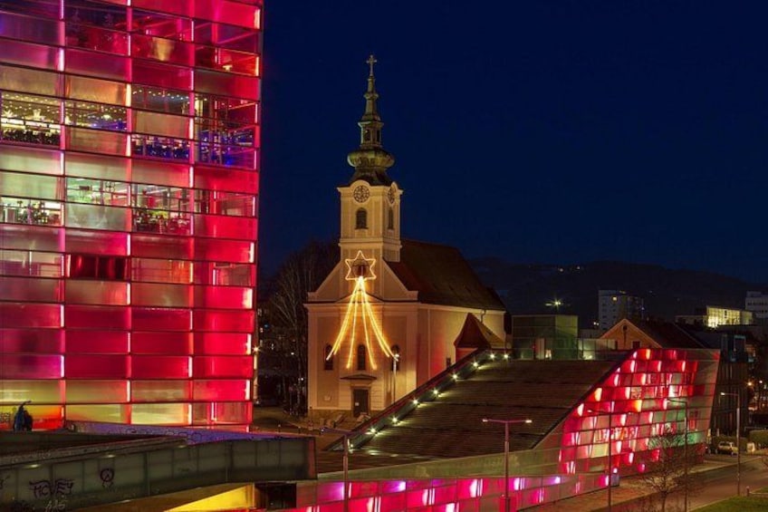 Un bâtiment illuminé, avec une église en arrière-plan. 1