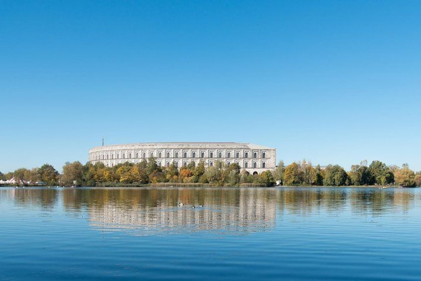 En stor, klassisk bygning med en symmetrisk facade, beliggende ved en rolig sø med klare spejlbilleder. 1