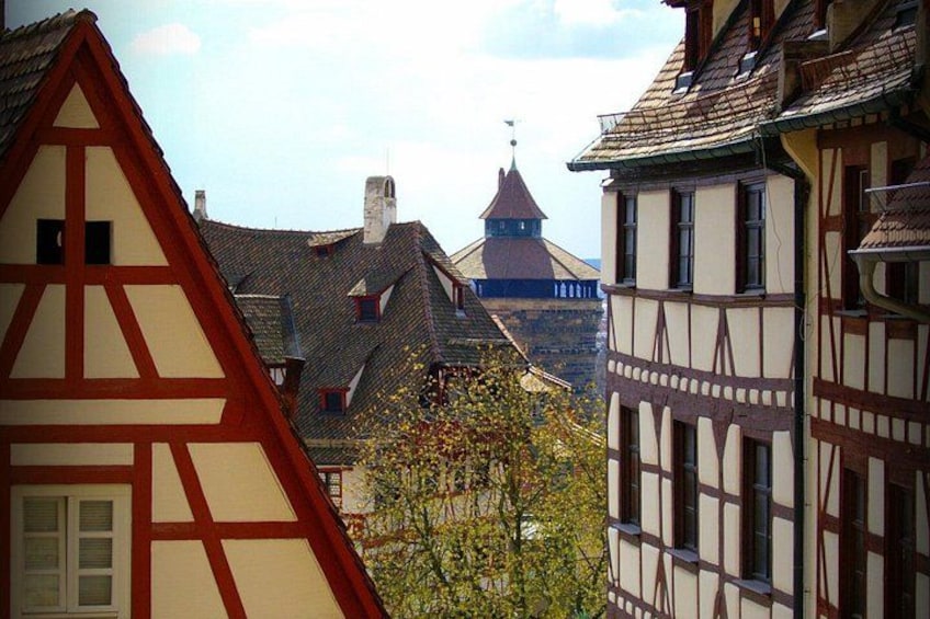 Une maison traditionnelle à colombages, avec un toit rouge en forme de triangle, une église surmontée d’une flèche, et un arbre aux fleurs jaunes. 3