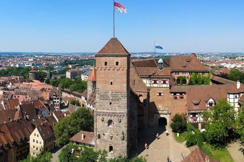 Ein historischer Turm mit einer Flagge, umgeben von traditionellen Gebäuden und blauem Himmel. 1