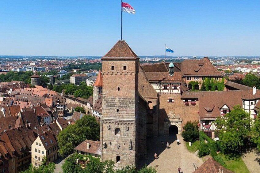 Une tour historique, surmontée d’un drapeau, entourée de bâtiments traditionnels et se dressant sous un ciel dégagé. 1