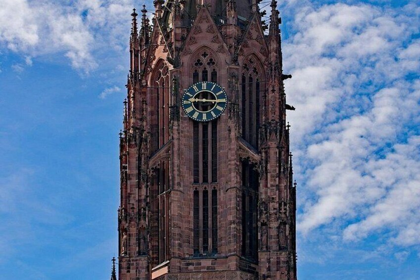 A tall Gothic-style clock tower with intricate architectural details against a partly cloudy sky. 3