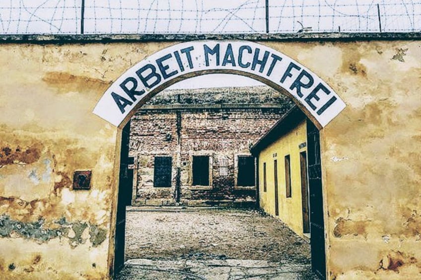 Un edificio fatiscente con un'insegna che recita 'ARBEIT MACHT FREI' e un ingresso sbarrato. 1