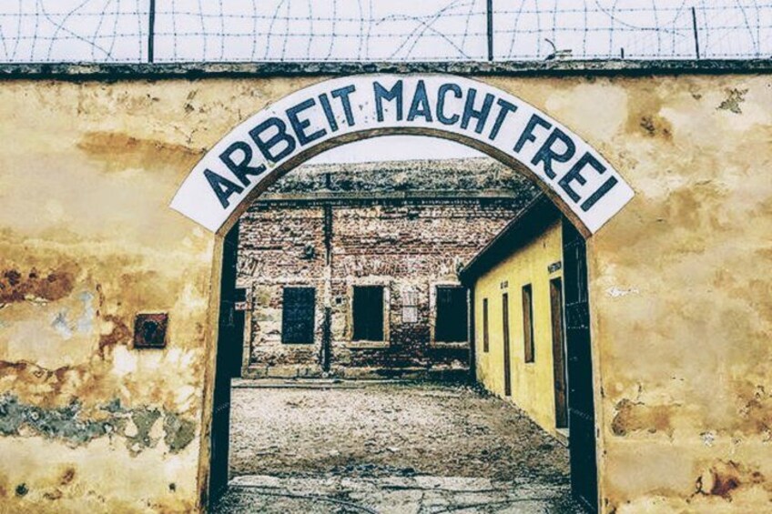 An archway with the inscription 'ARBEIT MACHT FREI' leading into a dilapidated building. 1