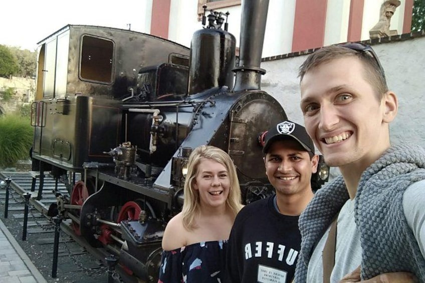 Een oude stoomlocomotief met drie personen die ervoor staan. 5