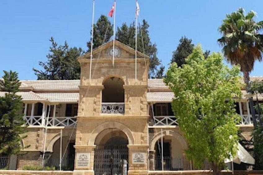 A stone building with a central archway, two flags on top, and a tree in the foreground. 2