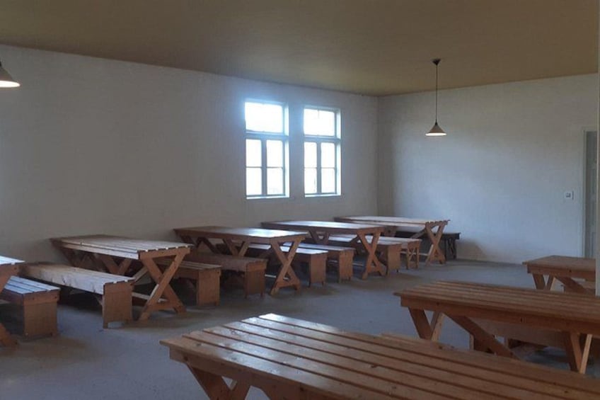 A classroom with wooden tables and benches, a window, and a hanging light fixture. 2